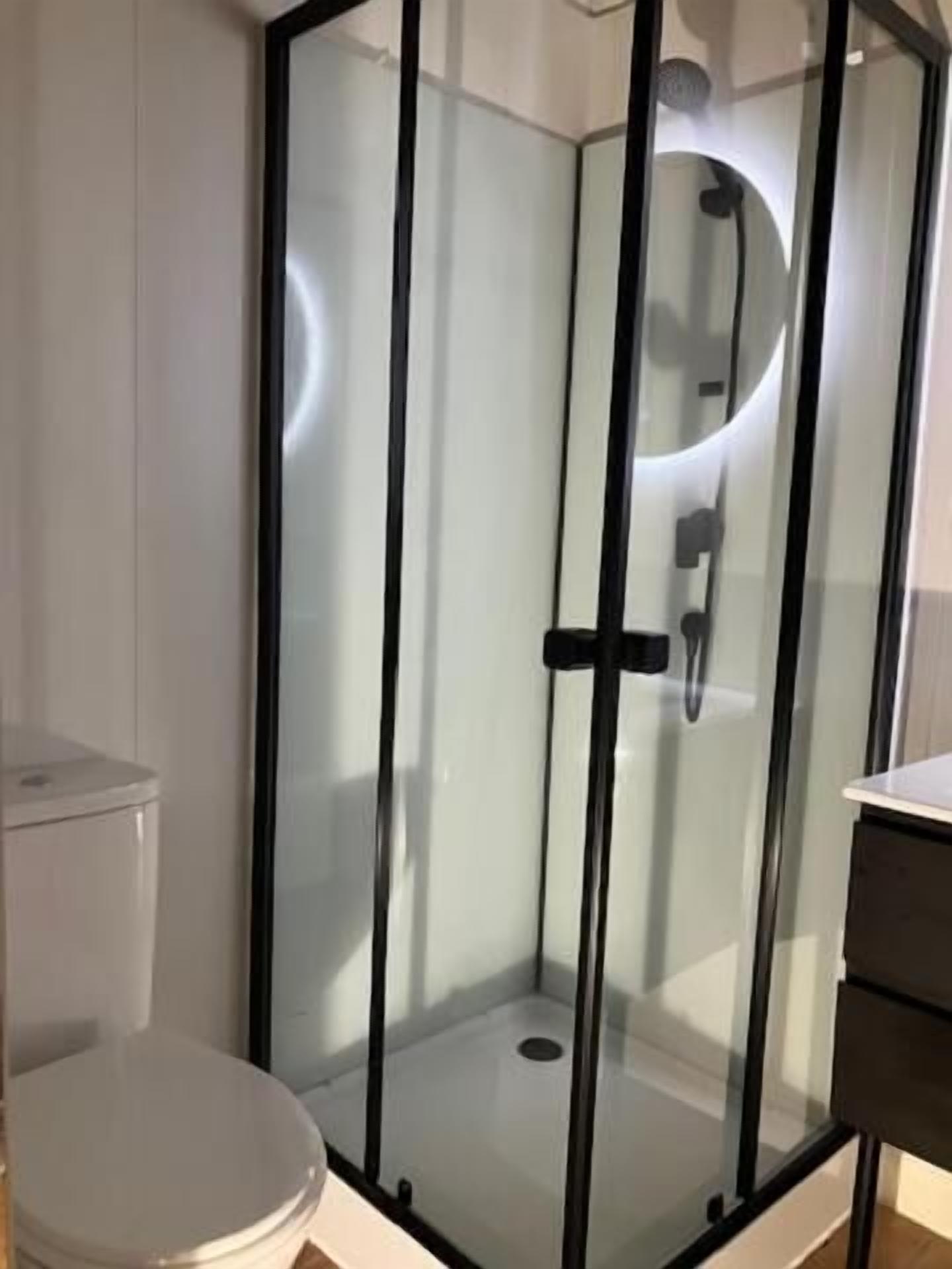Un baño con ducha separada por mampara de vidrio, inodoro y lavamanos.
