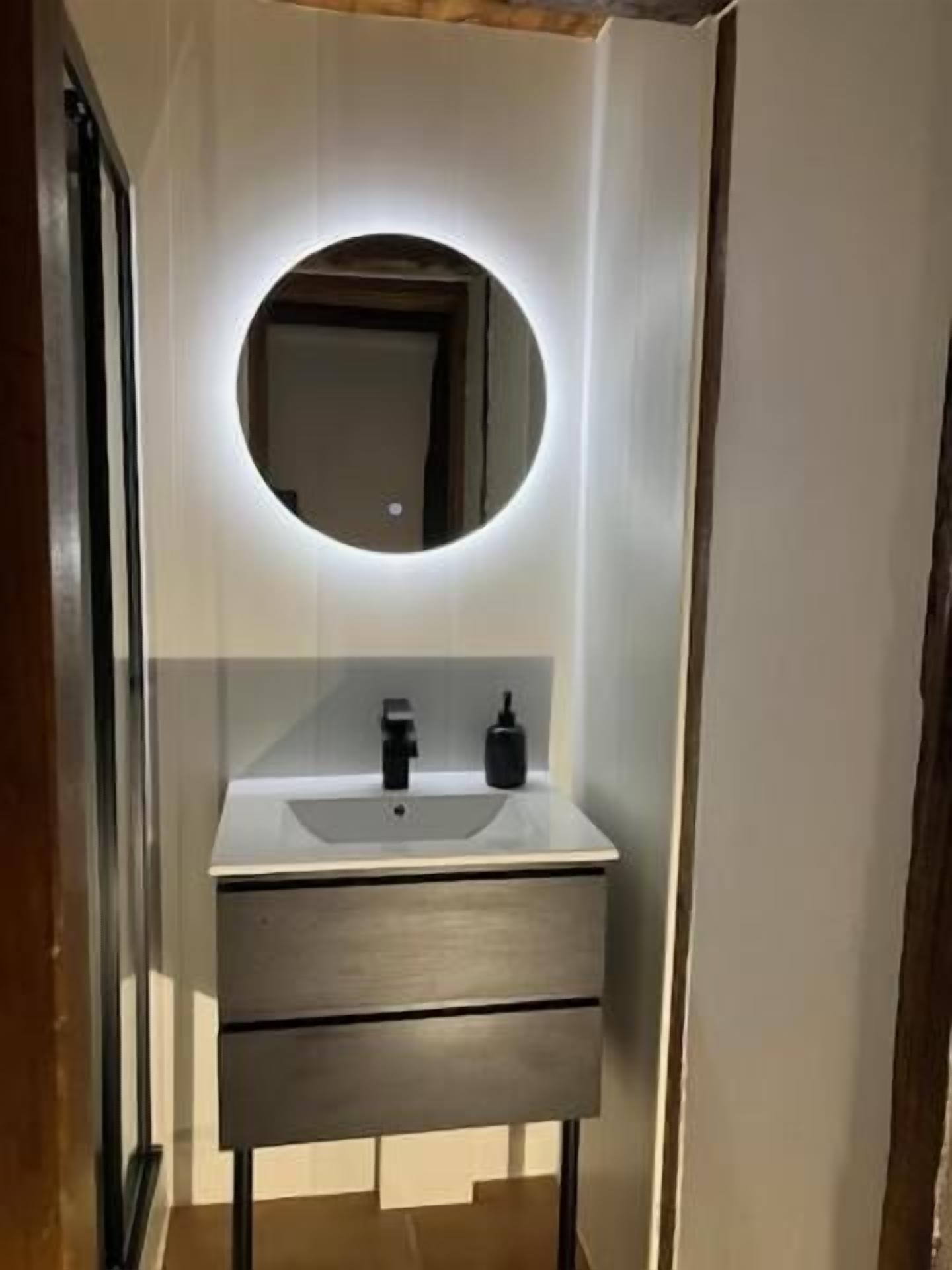 A bathroom with a white sink, a round mirror, and a black soap dispenser.