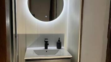 A bathroom with a white sink, a round mirror, and a black soap dispenser.