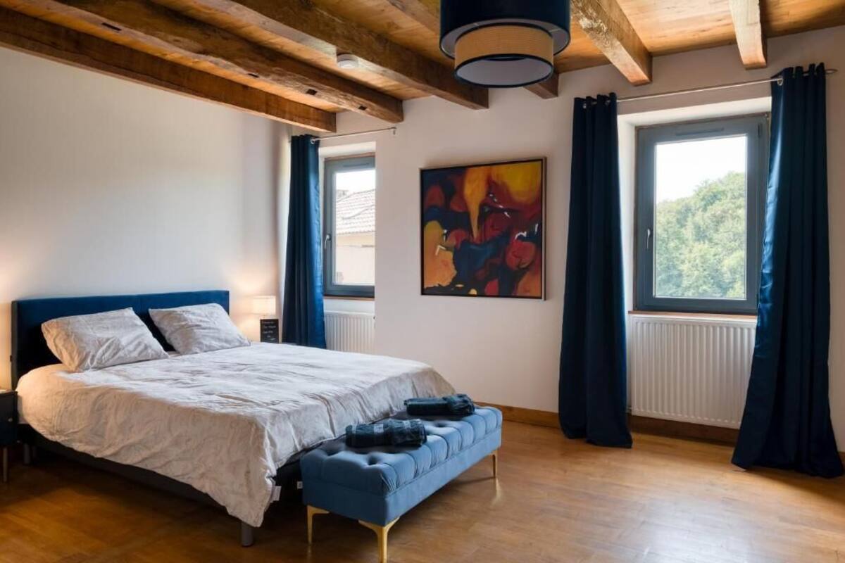 Une chambre à coucher avec un lit, un banc, des œuvres d’art et des fenêtres.