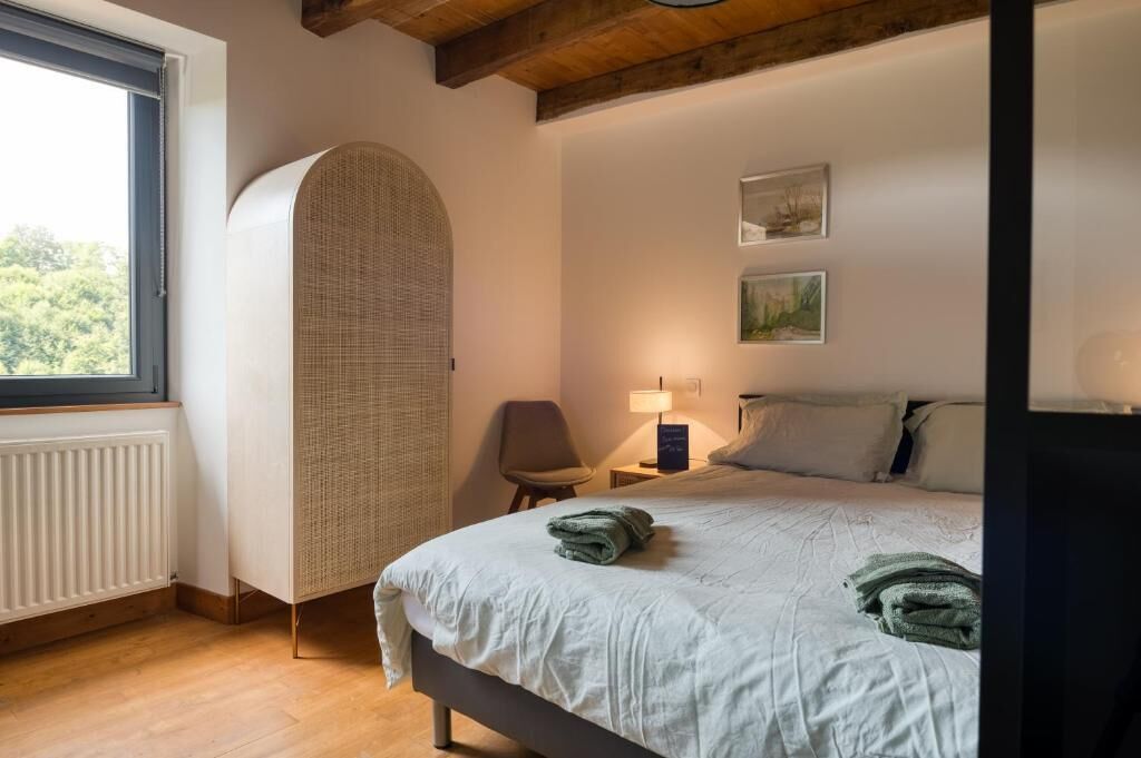 Ein Schlafzimmer mit einem Bett, einem Sessel, einer Lampe und einem Fenster.