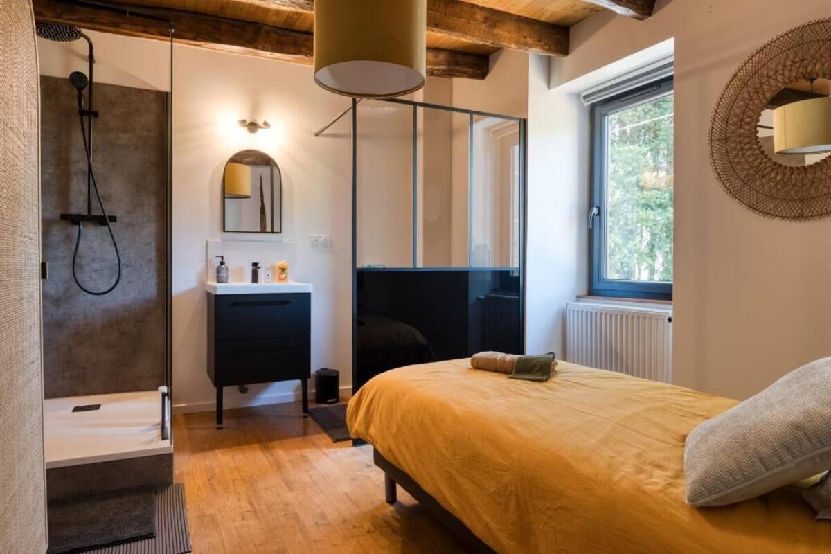Une chambre à coucher moderne comprenant un lit, une table de chevet, un miroir, une fenêtre et un espace douche.