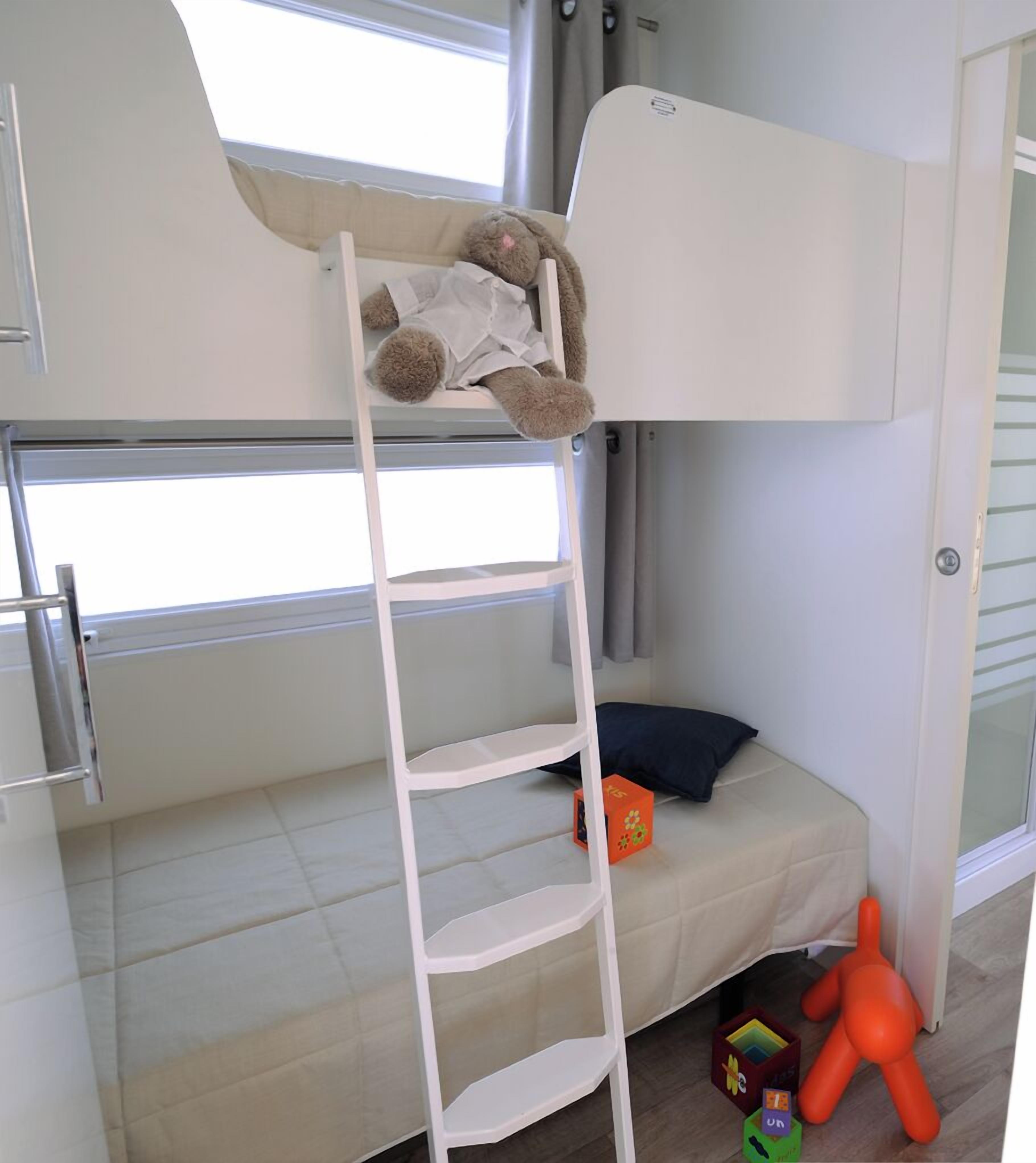 Una cama litera con escalera, una ventana, una puerta y juguetes en el suelo.