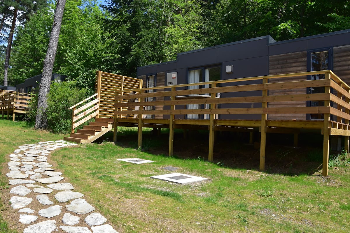 Una terraza moderna de madera que conduce a una cabaña, con un sendero de piedra.