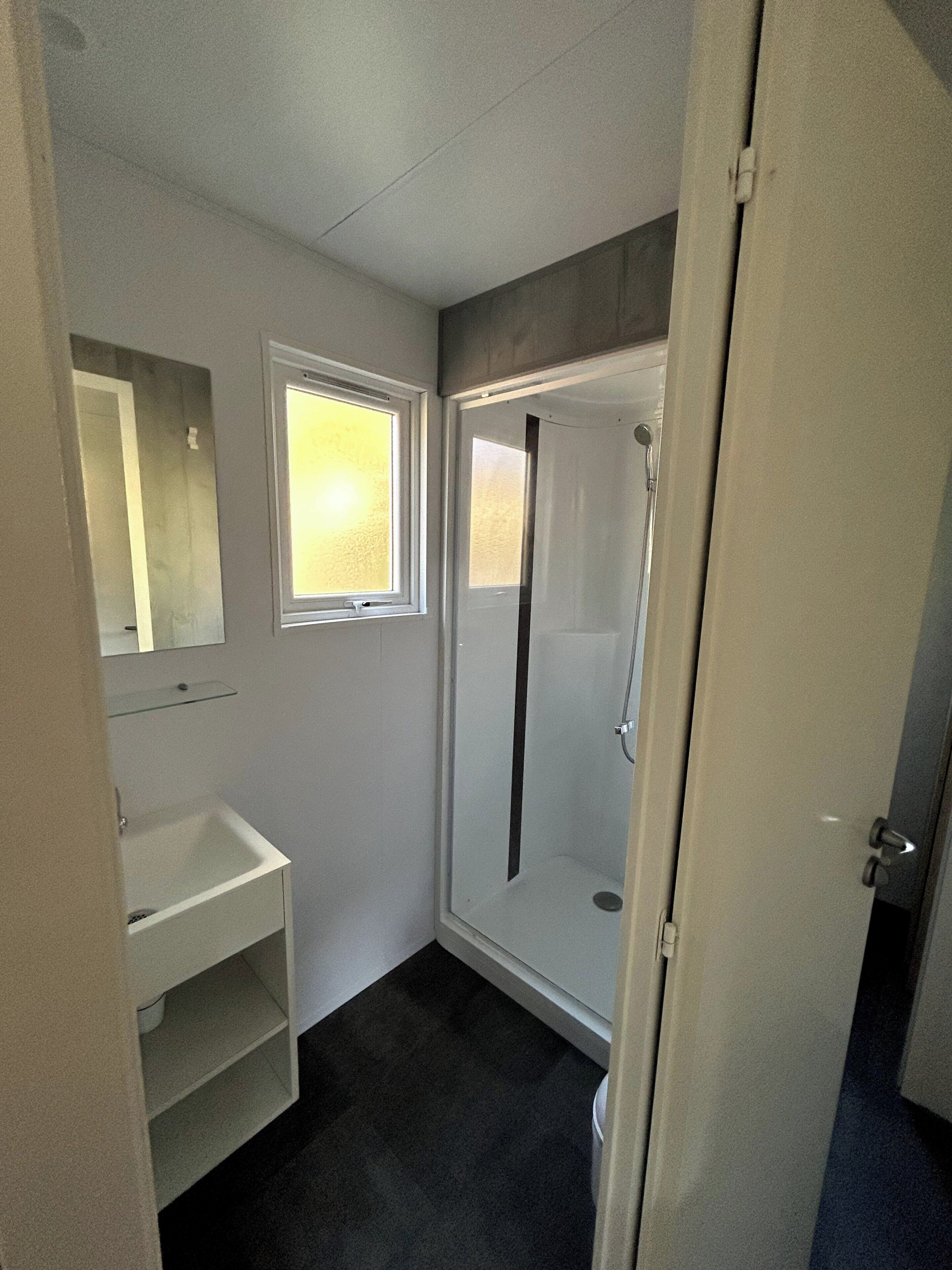 A small, enclosed bathroom with a shower, a sink, and a window.