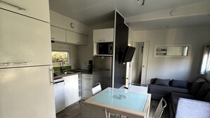 Cocina compacta con microondas, refrigerador y lavaplatos. Hay una mesa de comedor con sillas y un sofá en la sala.