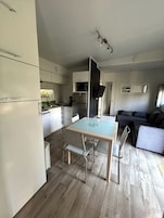 Cocina compacta con microondas, refrigerador y lavaplatos. Hay una mesa de comedor con sillas y un sofá en la sala.