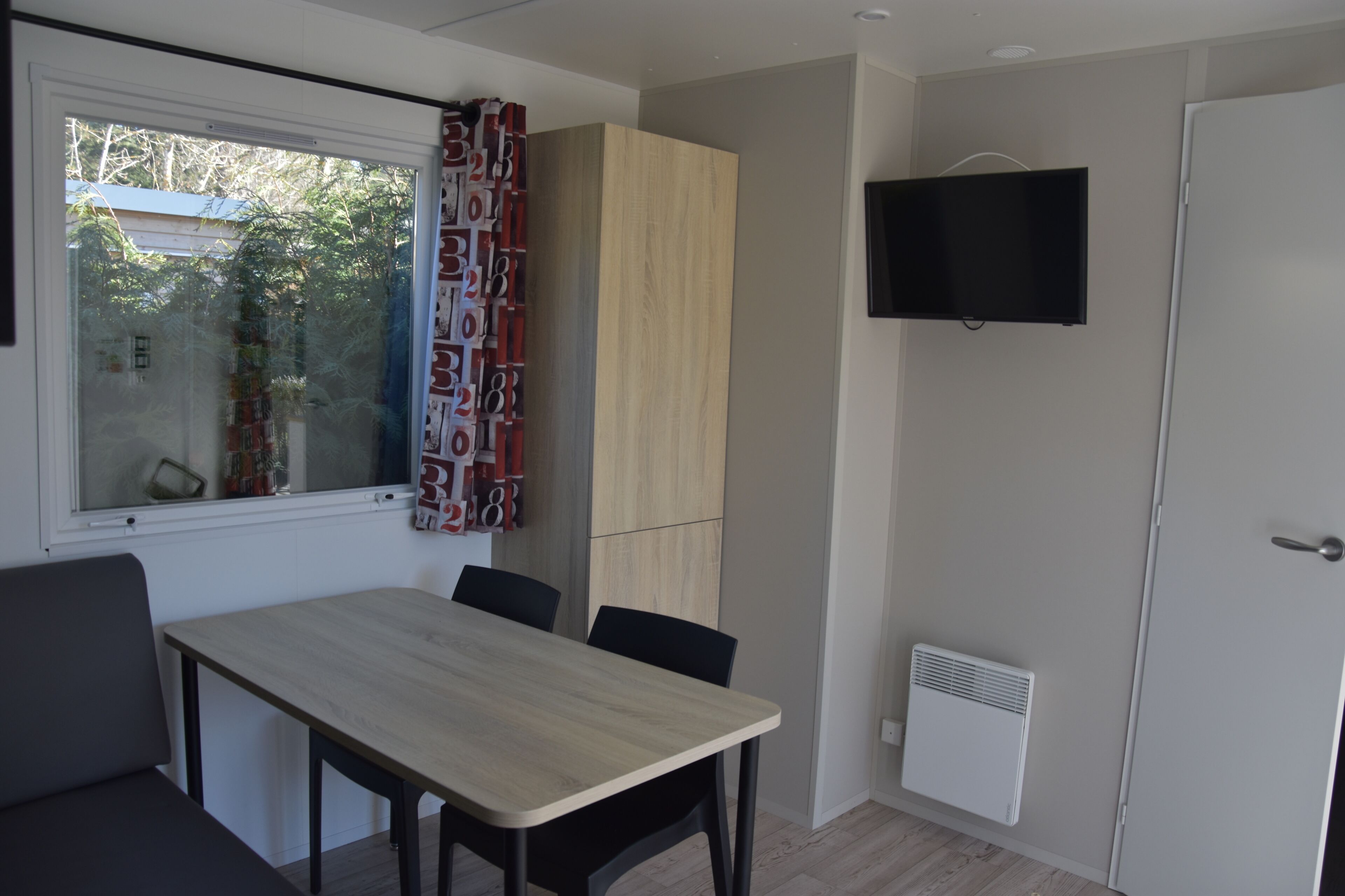Une chambre moderne équipée d’une table à manger, de chaises, d’un téléviseur fixé au mur et d’une armoire.