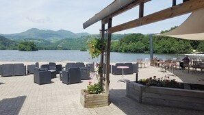 Un espacio al aire libre con mobiliario de mimbre y vistas a un lago y montañas.