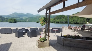 Un espacio al aire libre con mobiliario de mimbre y vistas a un lago y montañas.