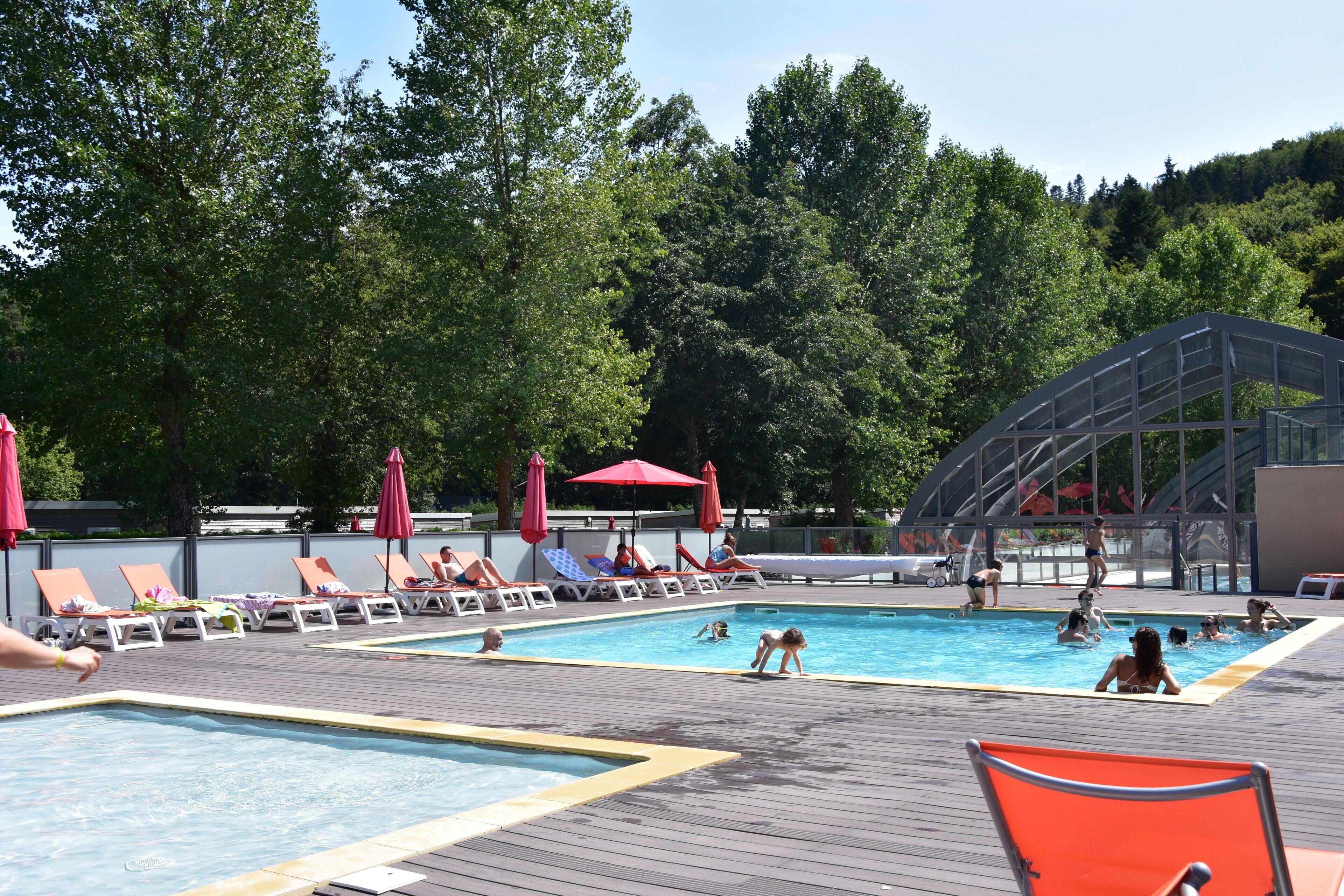 A pool area with lounge chairs and umbrellas, surrounded by trees.