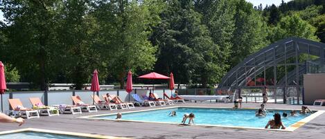 A pool area with lounge chairs and umbrellas, surrounded by trees.