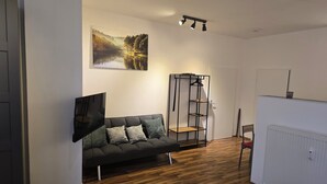Ein modernes Wohnzimmer mit einem dunklen Sofa, einem stehenden Bücherregal, einem Gemälde an der Wand und einer Heizung.