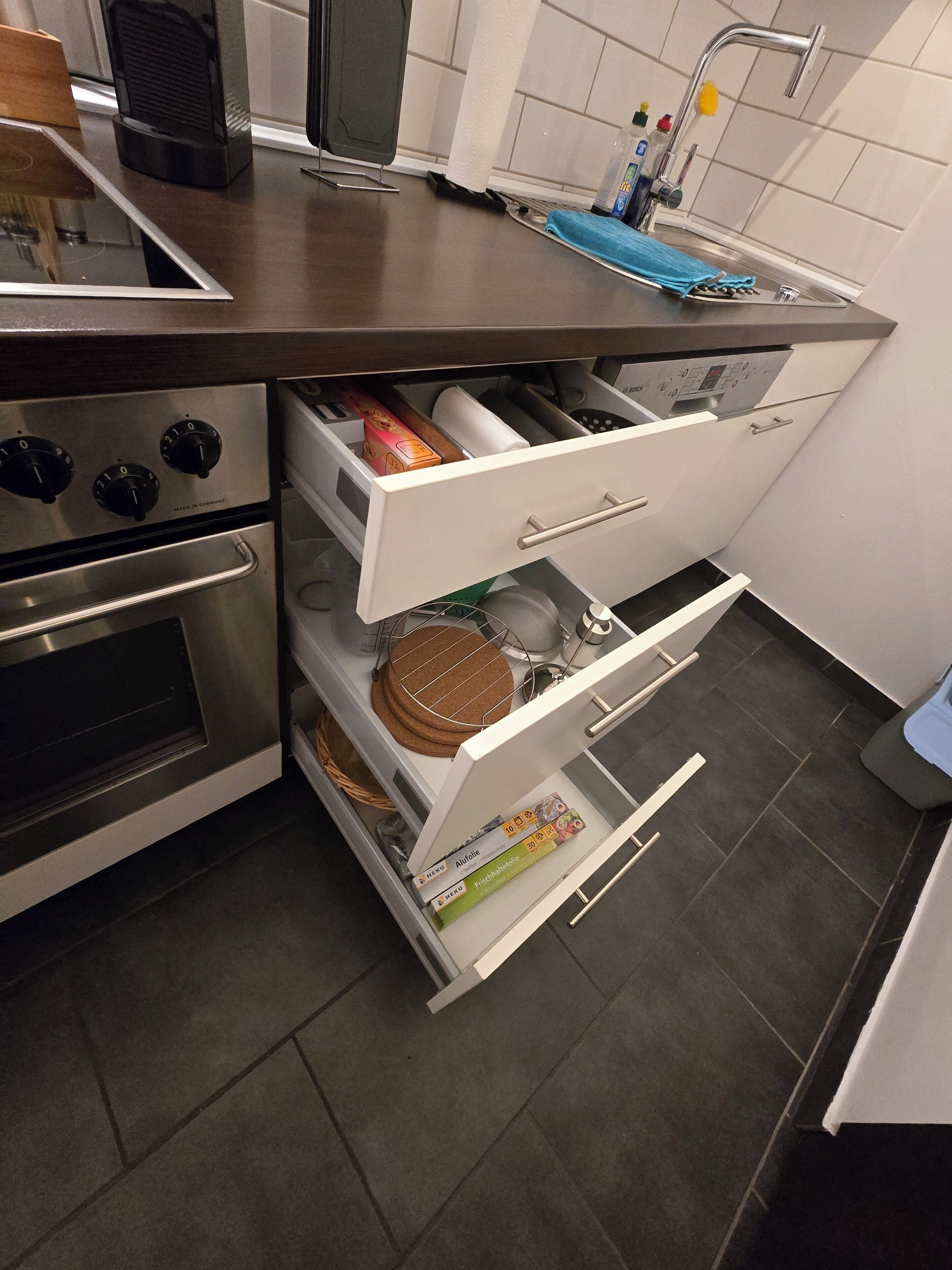 A kitchen with a built-in oven, a stainless steel range hood, a sink with a faucet, and a countertop with a toaster and a kettle.