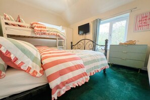 Un dormitorio con literas, televisor, cómoda y ventana con cortinas.
