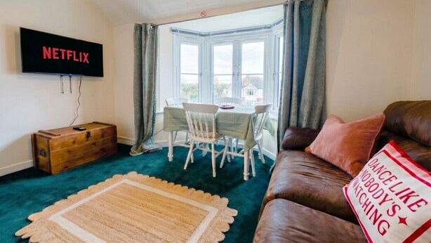 A living room with a television, a wooden chest, a dining table with chairs, a couch, and a window with curtains. - New Forest getaway just two minutes from the station (Hampshire)