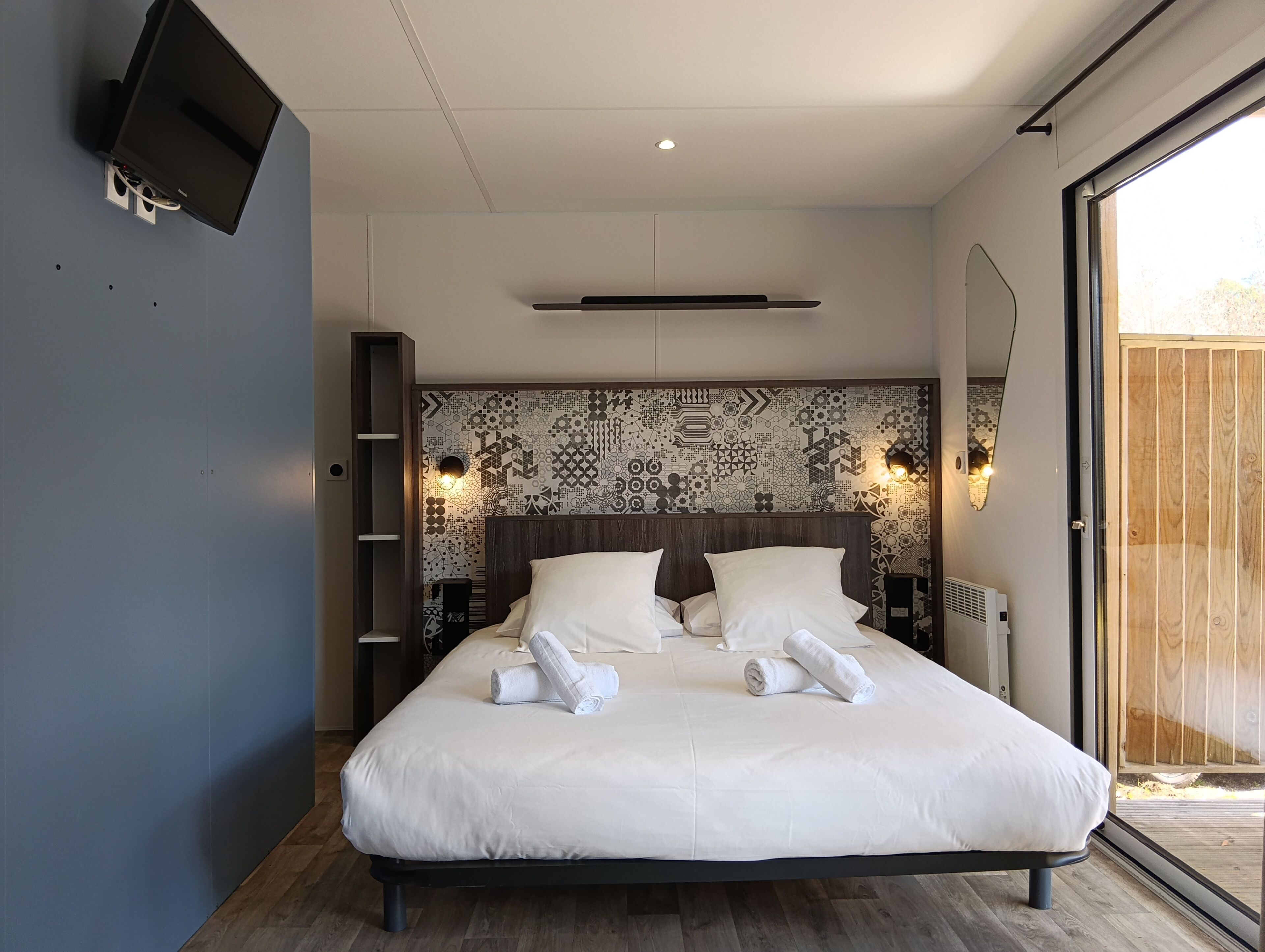 Un dormitorio moderno con una cama grande, un televisor montado en la pared y un diseño de pared estampado.