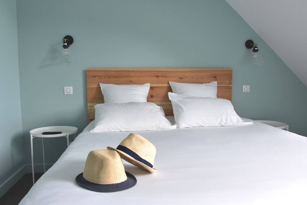 Een net opgemaakt bed met witte lakens, twee witte kussens en twee hoeden op het bed.