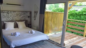 A bedroom with a large bed, a sliding glass door to a wooden deck, and a patterned wall. - Hôtel Lodge du Lac Chambon (Murol)