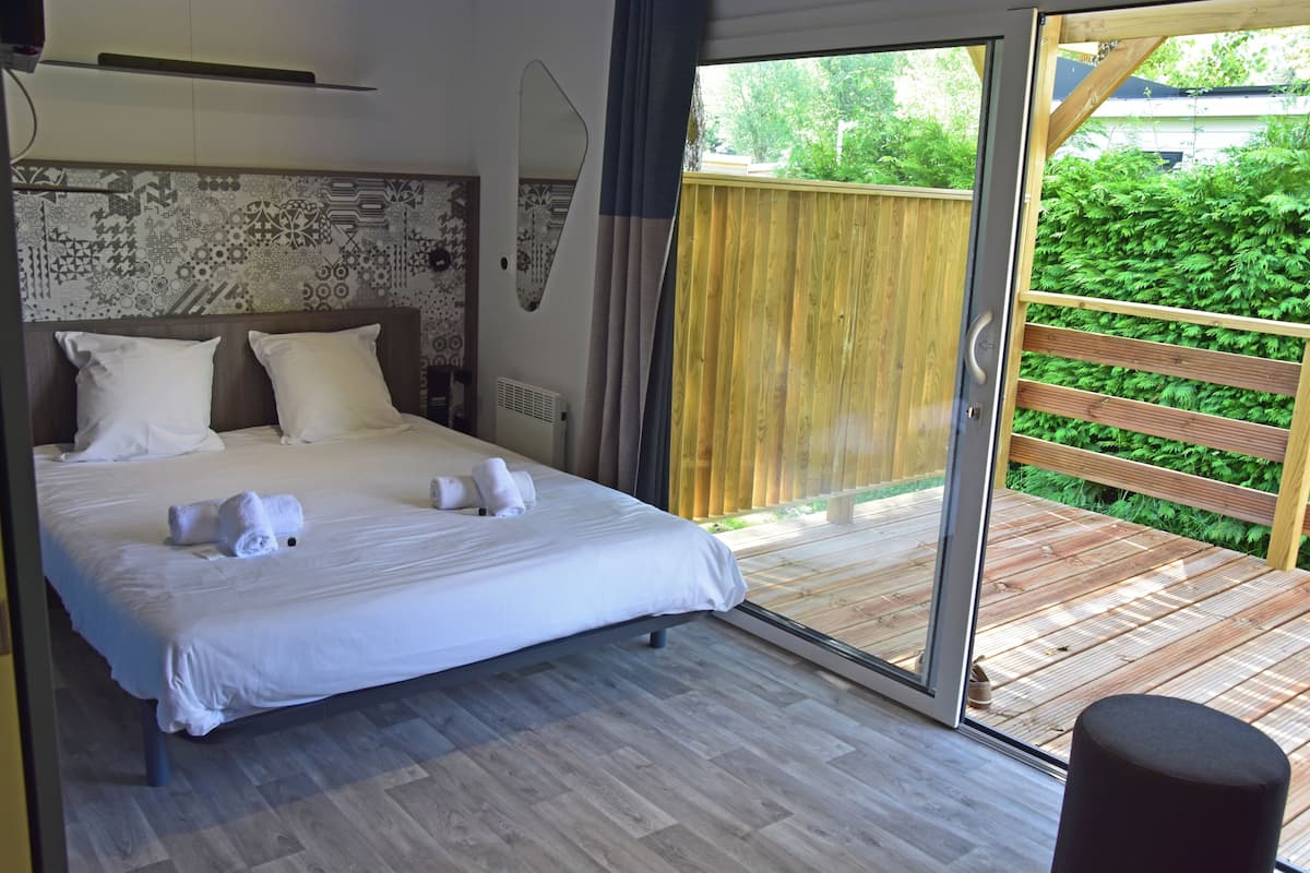 Een slaapkamer met een groot bed, een schuifdeur naar een houten terras en een behang met een patroon.