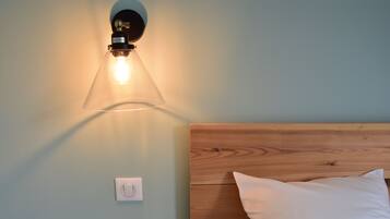 A room with a wooden headboard, a white pillow, a wall-mounted light fixture, and a light switch.