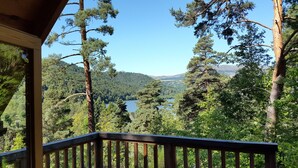 A wooden deck with a view of a lake surrounded by trees. - Hôtel Lodge du Lac Chambon (Murol)