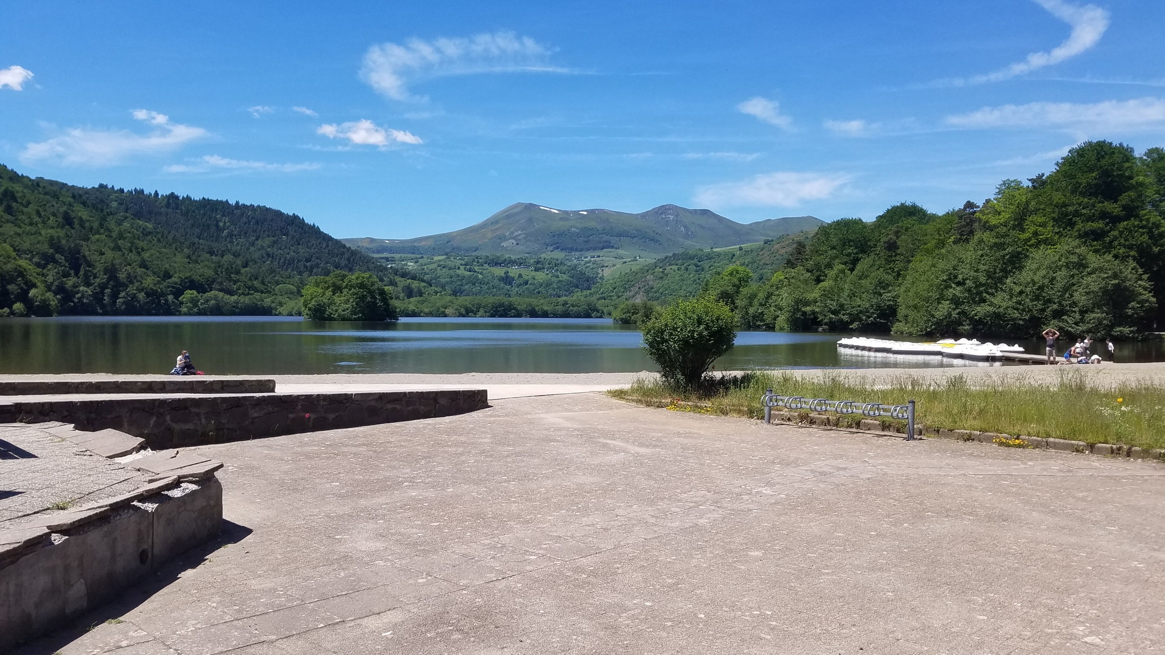 Zona junto a un lago con una plataforma de hormigón, una pequeña isla y una montaña al fondo.
