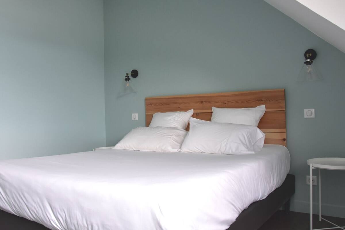 Een slaapkamer met een houten hoofdbord, wit beddengoed, een klein nachtkastje en wandlampen.