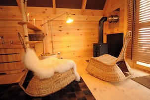 Un interior de madera con chimenea, mobiliario de mimbre y una lámpara colgante.