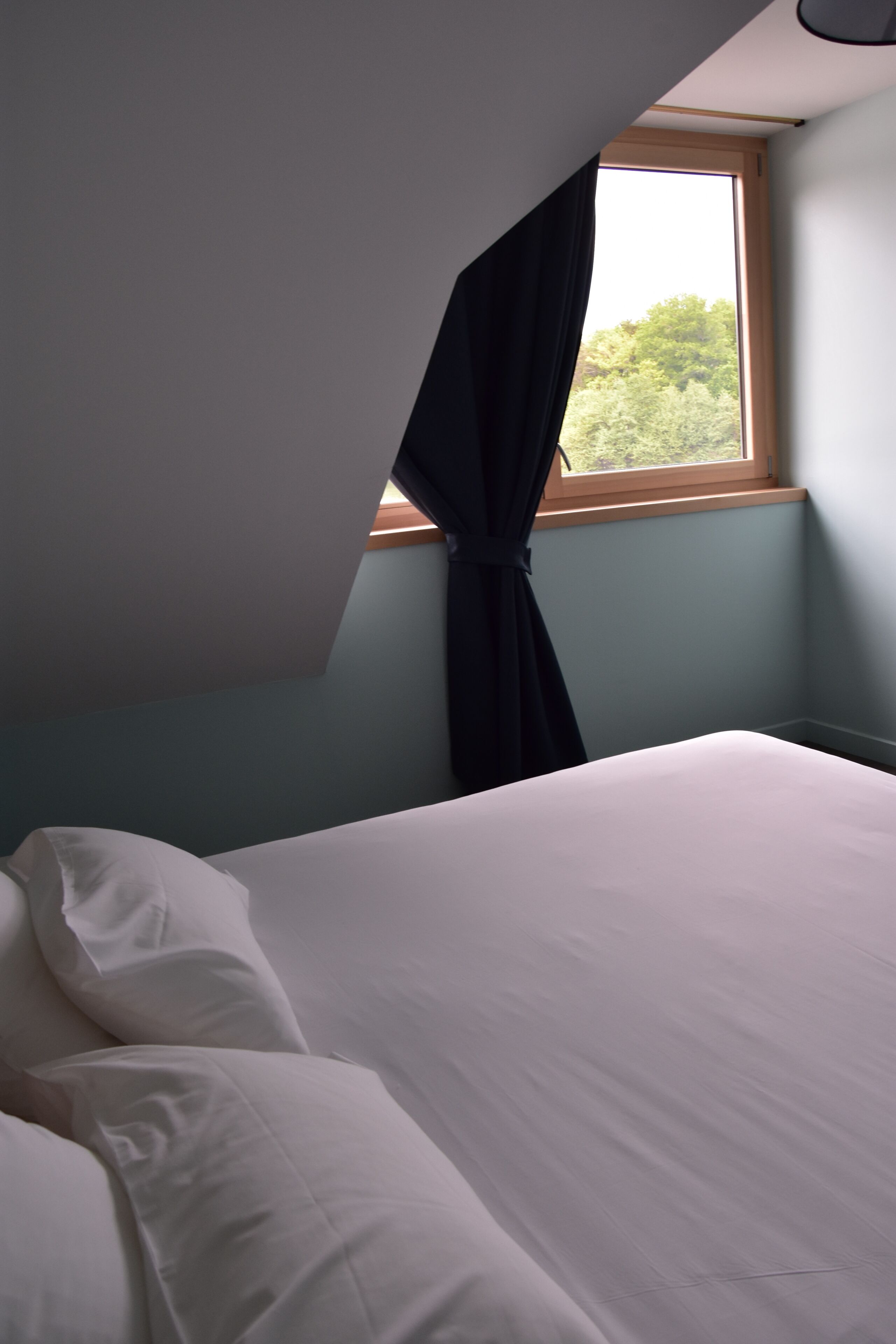 Un dormitorio con cama, ventana con cortinas y vista a árboles fuera.