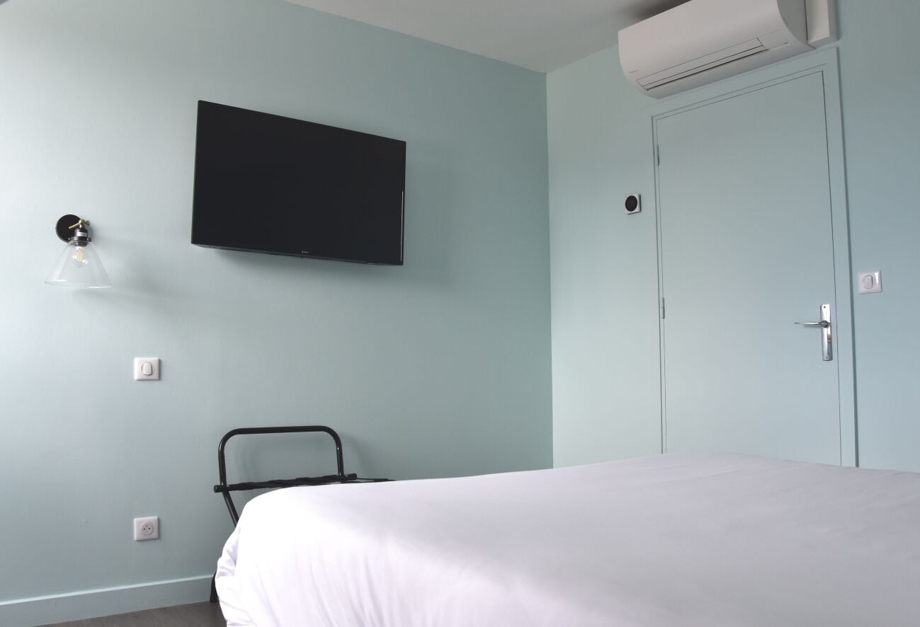 Une pièce comprenant un lit, un téléviseur fixé au mur, une lampe fixée au mur et une porte.