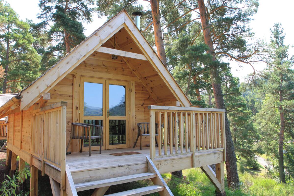 Een houten chalet met terras, grote ramen en schoorsteen.