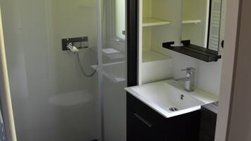 Een badkamer met een douchecabine van glas, een wit wastafelmeubel, een spiegel en een toilet.