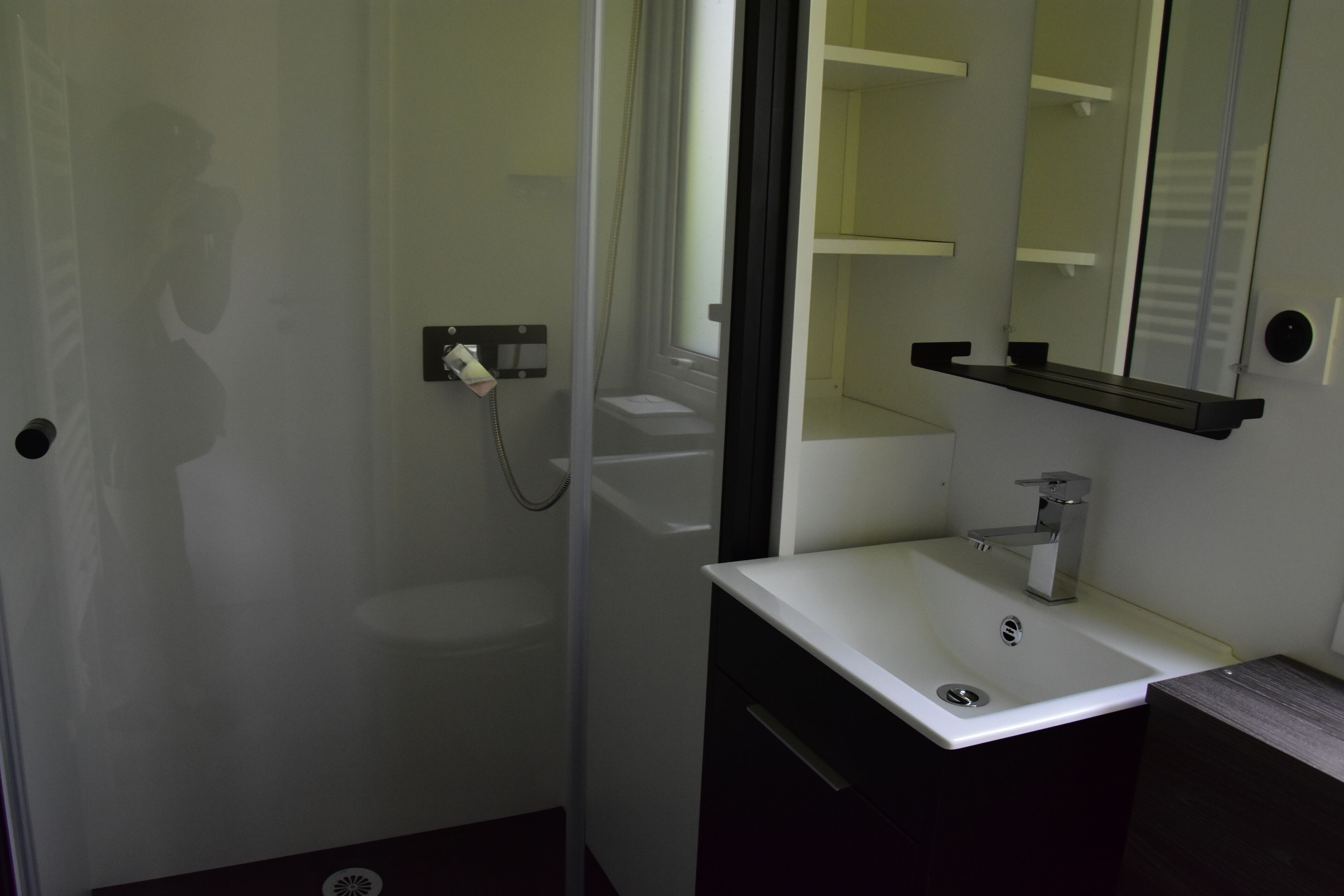 Een badkamer met een wit wastafelmeubel, een spiegel en een douchegedeelte.