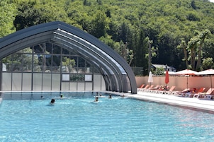 Una piscina con zona cubierta, rodeada de sillas de descanso y sombrillas.