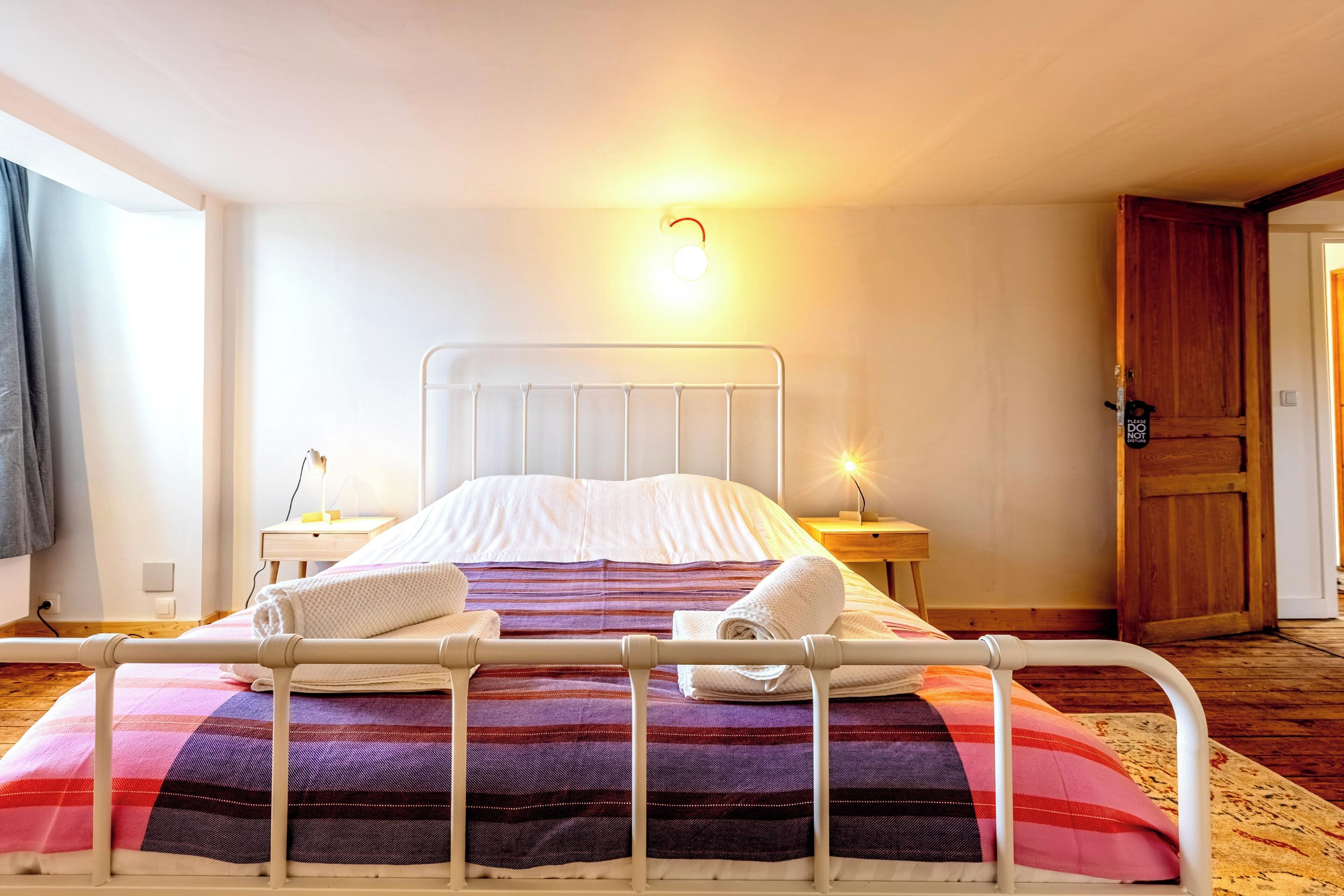 Een bed met een metalen frame, een nachtkastje met een lamp en een houten deur.