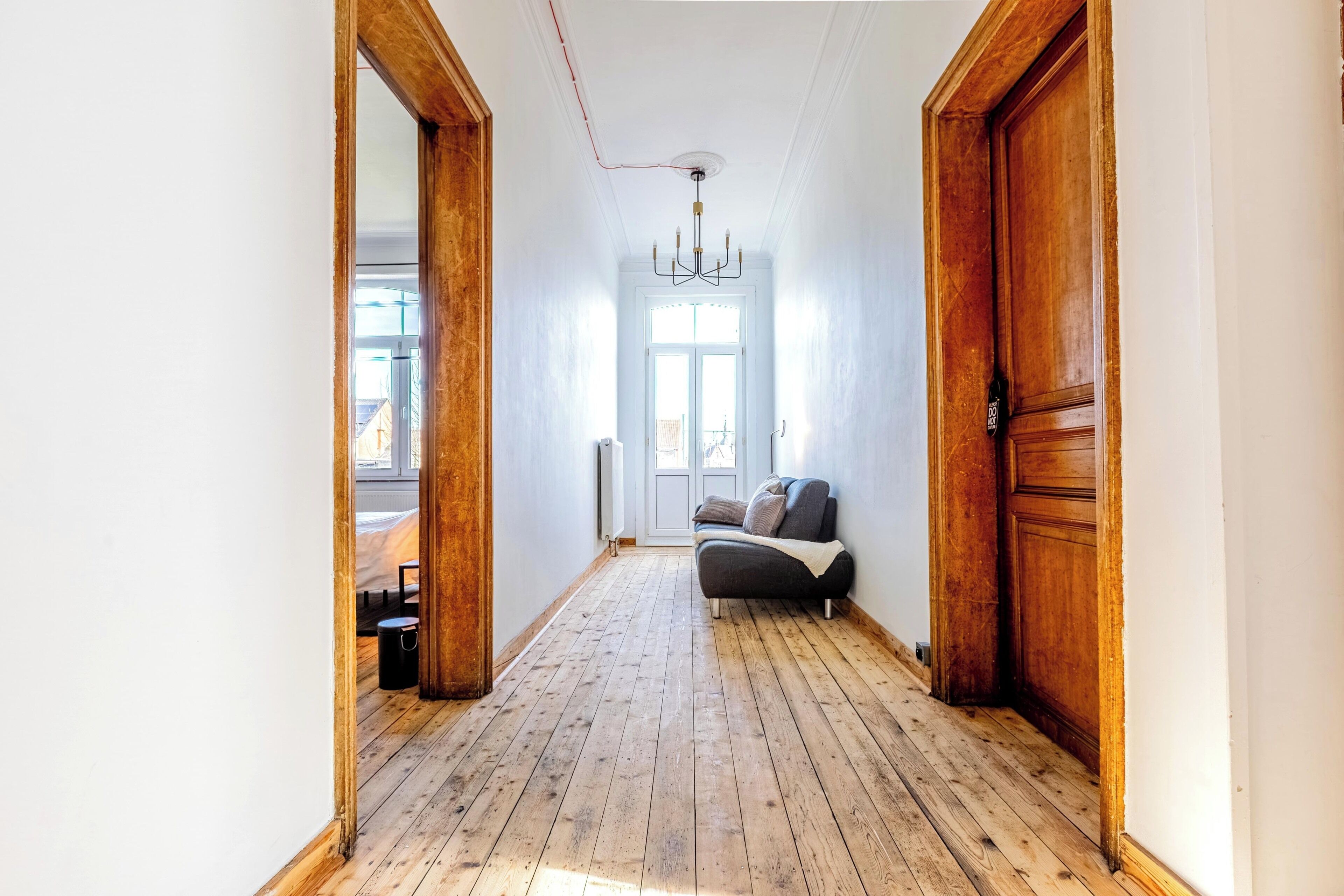 Un pasillo con pisos de madera, un candelabro y un sofá con cojines.