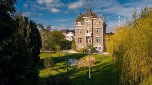 En stor, historisk bygning med flere etager, et markant tårn og en velholdt have med et bassin.