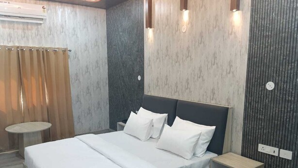 A modern bedroom with a bed, bedside tables, and an air conditioning unit. - AN PERFECT STAYS IN THE LAP OF ARAVALI HILLS (Gurugram)