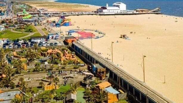 Eine Küstenlandschaft mit Strand, einer Mole und einem weißen Gebäude mit schrägem Dach.