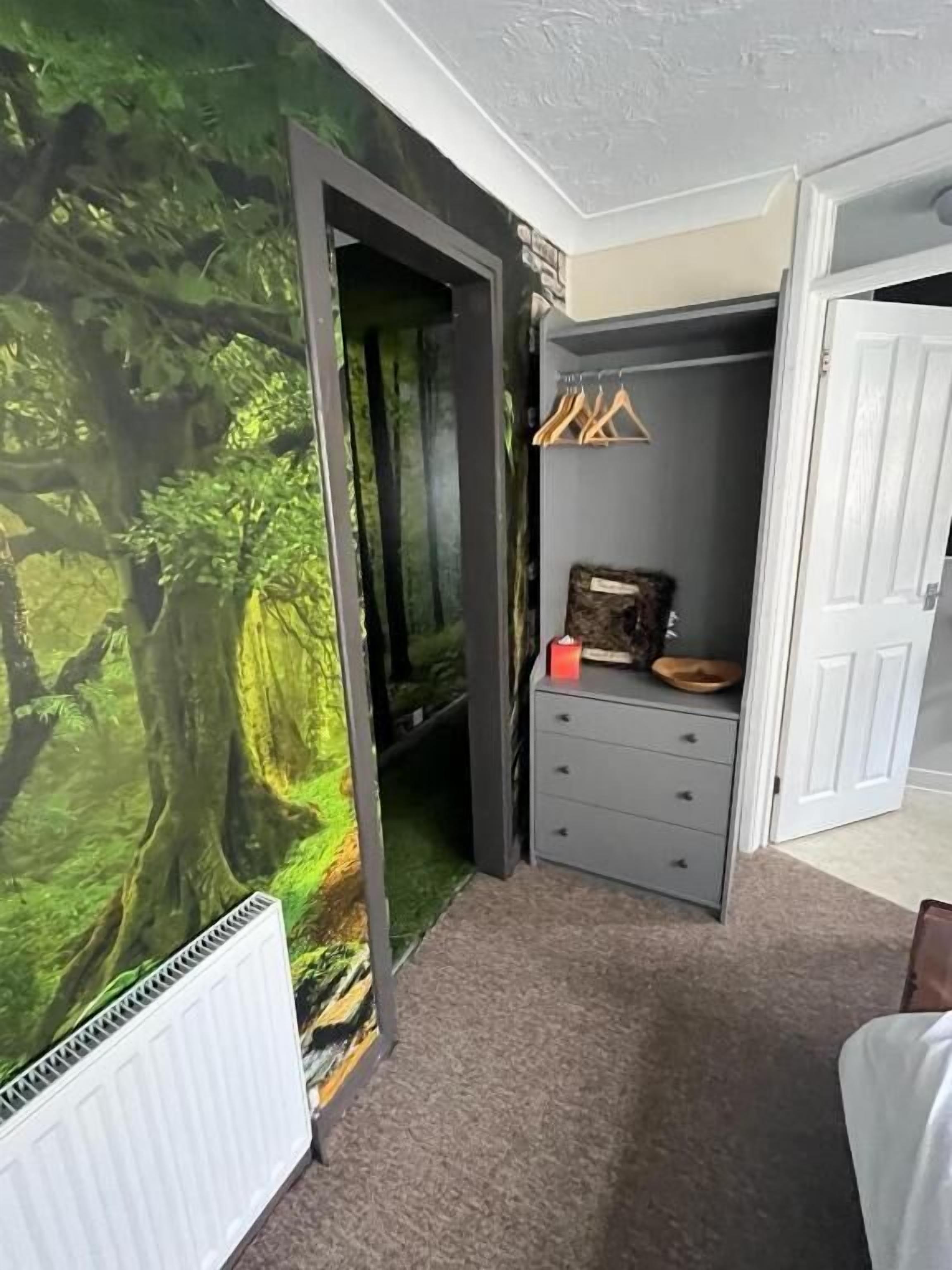 Una stanza con un murale raffigurante una foresta, un comò grigio e un termosifone bianco.