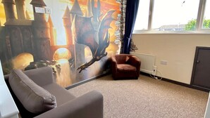 Ein Zimmer mit einer großen Drachenmalerei, einem braunen Sessel, einem Heizkörper und einem Fenster mit Blick zum Himmel.
