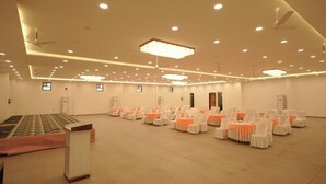 A spacious hall with rows of tables and chairs, a podium, and ceiling fans. - The Manrals Resort (Ramnagar)