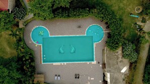 An aerial view of a swimming pool with two smaller pools, surrounded by a paved area with lounge chairs and a few trees. - The Manrals Resort (Ramnagar)