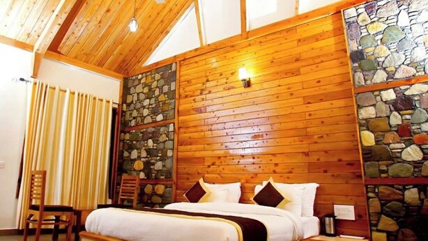 A wooden-paneled bedroom with a stone accent wall, a bed with pillows, a nightstand, and a chair. - The Manrals Resort (Ramnagar)