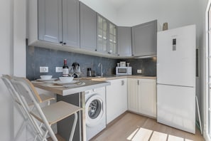 Een compacte keuken met grijze kastjes, een wasmachine, een magnetron en een Bosch koelkast.