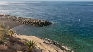 A coastal view with a rocky breakwater, clear blue water, and a sandy beach.