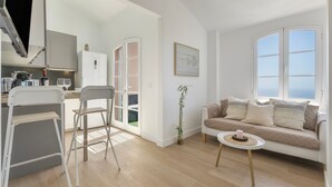 A modern living room with a sofa, a small round table, and a kitchen area with a fridge and cabinets.