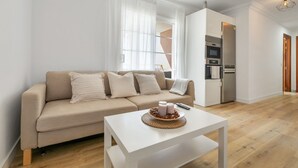 Ein modernes Wohnzimmer mit einer Couch, einem Couchtisch und einer Küchenzeile inklusive Geräte.
