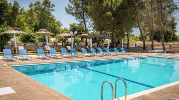 A swimming pool with lounge chairs and umbrellas, surrounded by trees.